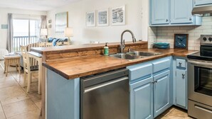 A modern kitchen with blue cabinets, a stainless steel sink, and a built-in oven. - Captain's Walk III 1C - Oceanfront in Garden City Beach (Garden City)