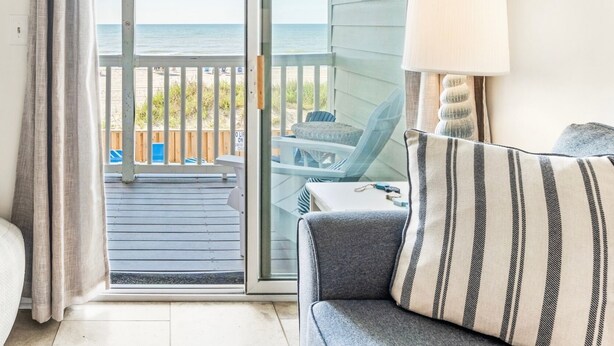 A room with a view of the beach, a sliding glass door, a sofa, a lamp, and a small table. - Captain's Walk III 1C - Oceanfront in Garden City Beach (Garden City)