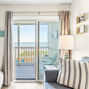 A room with a view of the beach, a sliding glass door, a sofa, a lamp, and a small table. - Captain's Walk III 1C - Oceanfront in Garden City Beach (Garden City)