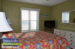 Une chambre à coucher comprenant un lit, une télévision, une commode et une fenêtre avec des stores.
