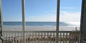 A beach view from a balcony with a pool and lounge chairs.