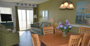 A dining area with a wooden table and chairs, a vase with flowers, and a painting on the wall.