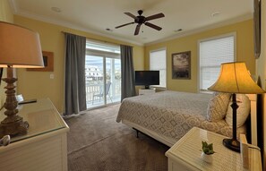 A hotel room with a bed, a desk, a television, a ceiling fan, and a view of the outside. - Crabby Cabin A - Walk to Beach (Marshfront) in Garden City Beach (Garden City)