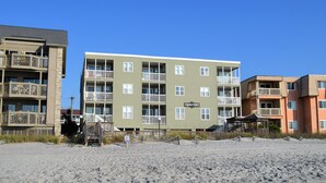 Un edificio a più piani con balconi, una spiaggia in primo piano e un cartello che indica 'Captain's Walk'.