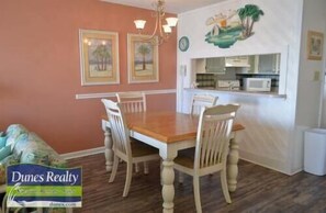A dining area with a wooden table and four chairs, a chandelier, and framed artwork on the walls.