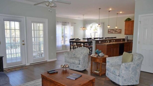 A spacious living room with a wooden coffee table, two patterned armchairs, a dining area with a kitchen in the background, and a ceiling fan. - Bikini Bottom - Walk to Beach in Surfside Beach (Surfside Beach)