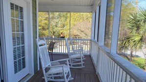 A porch with white rocking chairs and a view of trees and a lawn. - Bikini Bottom - Walk to Beach in Surfside Beach (Surfside Beach)