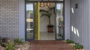 Une entrée moderne avec une porte en verre, un chemin en bois et une plante en pot.