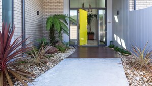 Une entrée moderne avec un chemin en béton, des plantes en pot et une porte jaune.