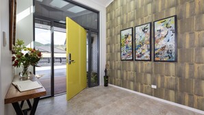 Un intérieur moderne avec une porte jaune, une table en bois ornée d’un vase et trois tableaux abstraits accrochés au mur.