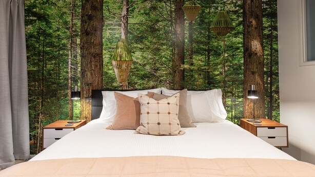 Une chambre à coucher avec un lit, des oreillers, des tables de chevet et un papier peint sur le thème de la forêt.