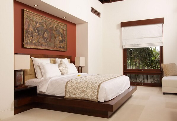 Un dormitorio con una cama grande, una mesita de noche, una lámpara de noche, una ventana con vistas al verdor y un cuadro colgado en la pared.