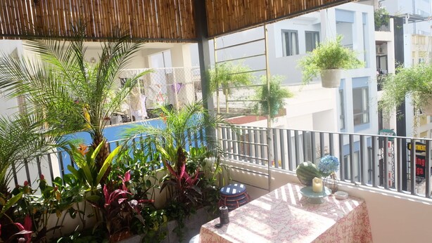 Balcón con vista a una zona residencial, que incluye una mesa con mantel floral y plantas en macetas.
