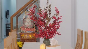 Un comedor con una mesa dispuesta para dos, un florero decorativo con bayas rojas, una vela encendida y una estatua sobre una mesita.