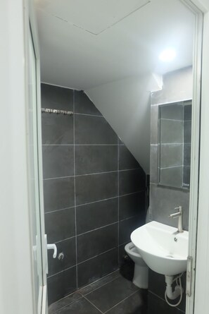 Un baño con azulejos oscuros, un lavabo blanco y un inodoro.