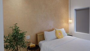 Una habitación de hotel con cama, mesita de noche, planta en maceta y ventana con vistas.