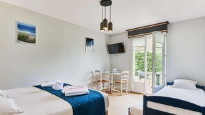 Quarto de hotel com duas camas, uma mesa de jantar, cadeiras, uma televisão e uma janela grande.