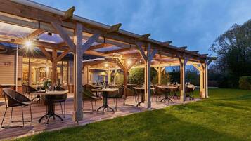 An outdoor patio with wooden tables and chairs, a grill, and a covered seating area.