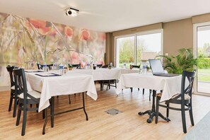 A conference room with tables, chairs, a laptop, and a large window with a view of greenery.