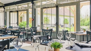 En restaurang med bord som är dukade för middag, stora fönster och utsikt över omgivningen.