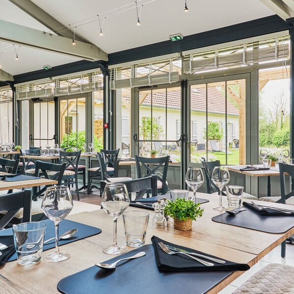 Ein Restaurant mit gedeckten Tischen, großen Fenstern und Blick ins Freie.