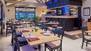 Restaurante com várias mesas, cadeiras, um espaço de bar e vista pela janela grande.