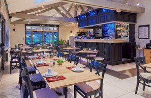 A restaurant with multiple tables, chairs, a bar area, and a view through large windows. - Domaine Les Saules (Favieres)