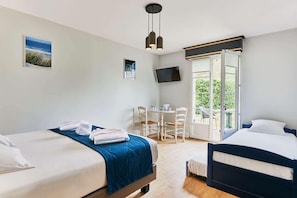 A hotel room with two beds, a dining table, chairs, a TV, and a large window.