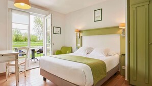 Quarto com cama, escrivaninha, cadeira e vista para o exterior.