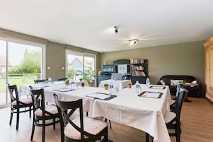 Un comedor con mesas dispuestas para seis comensales, sillas, una estantería y un televisor.