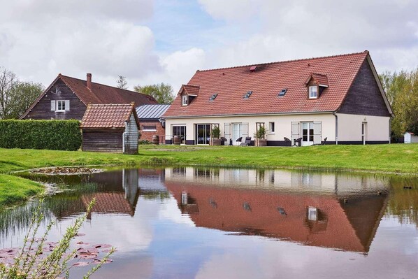 A traditional house with a pond in front, a grassy area, and a clear sky.