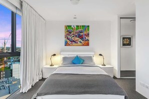 A modern hotel room with a large bed, two bedside tables, a city view, and a colorful abstract painting above the bed. - View from the Top ~ 2Bed, 2Bath, 2Parking, Balcony (South Brisbane)
