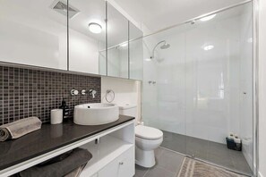 Et moderne badeværelse med et brusekabine i glas, en hvid vask og et toilet.