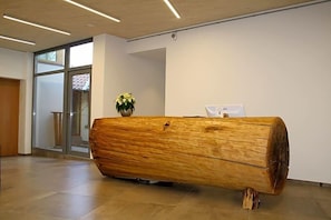 A reception desk made of a large log, a potted plant, and a glass door leading to an outdoor area.
