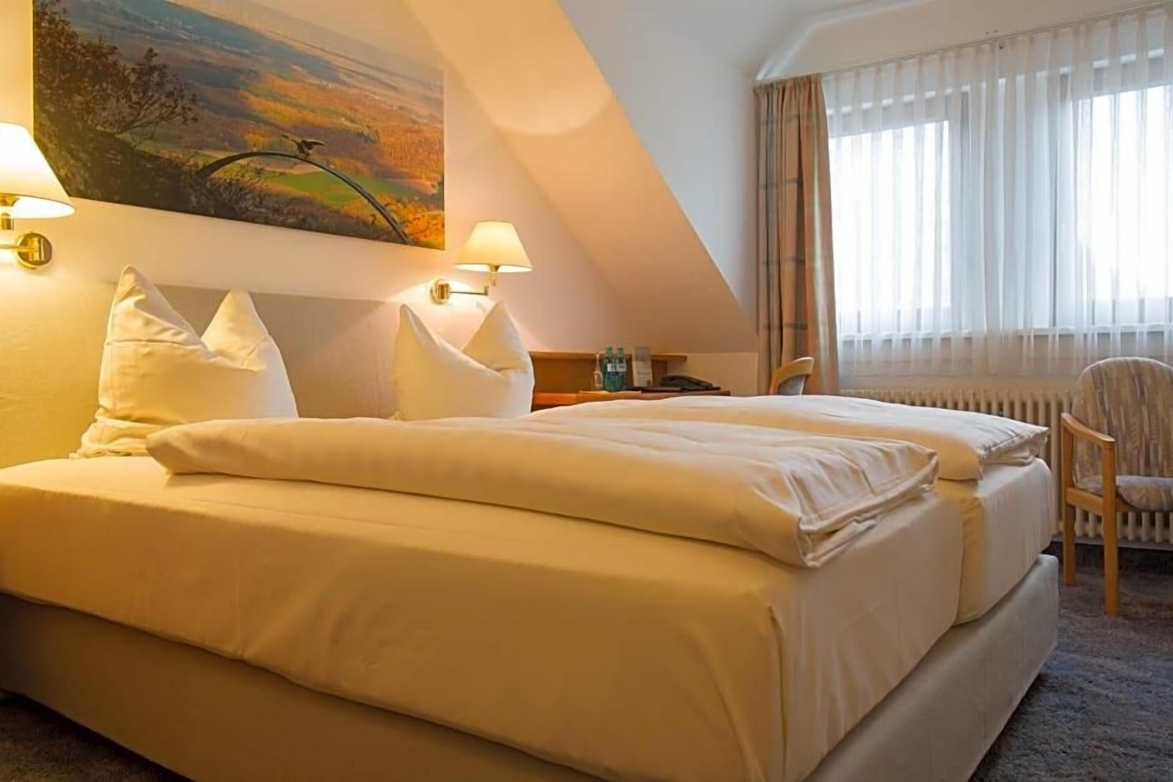 Ein Hotelzimmer mit einem großen Bett, einem Nachttisch, einem Sessel und einem Gemälde an der Wand.