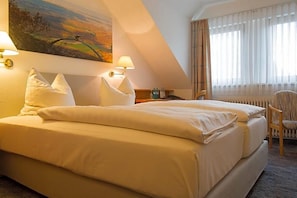 A hotel room with a large bed, a nightstand, a chair, and a painting on the wall.