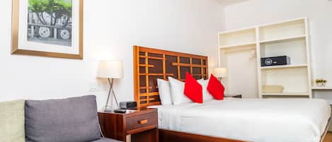 Habitación de hotel con cama, sofá, cabecero de madera, mesitas de noche, lámpara y un cuadro en la pared.