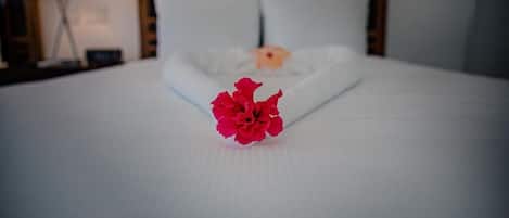 Una cama bien hecha con una flor roja en el centro, una almohada blanca y un cabecero de madera.