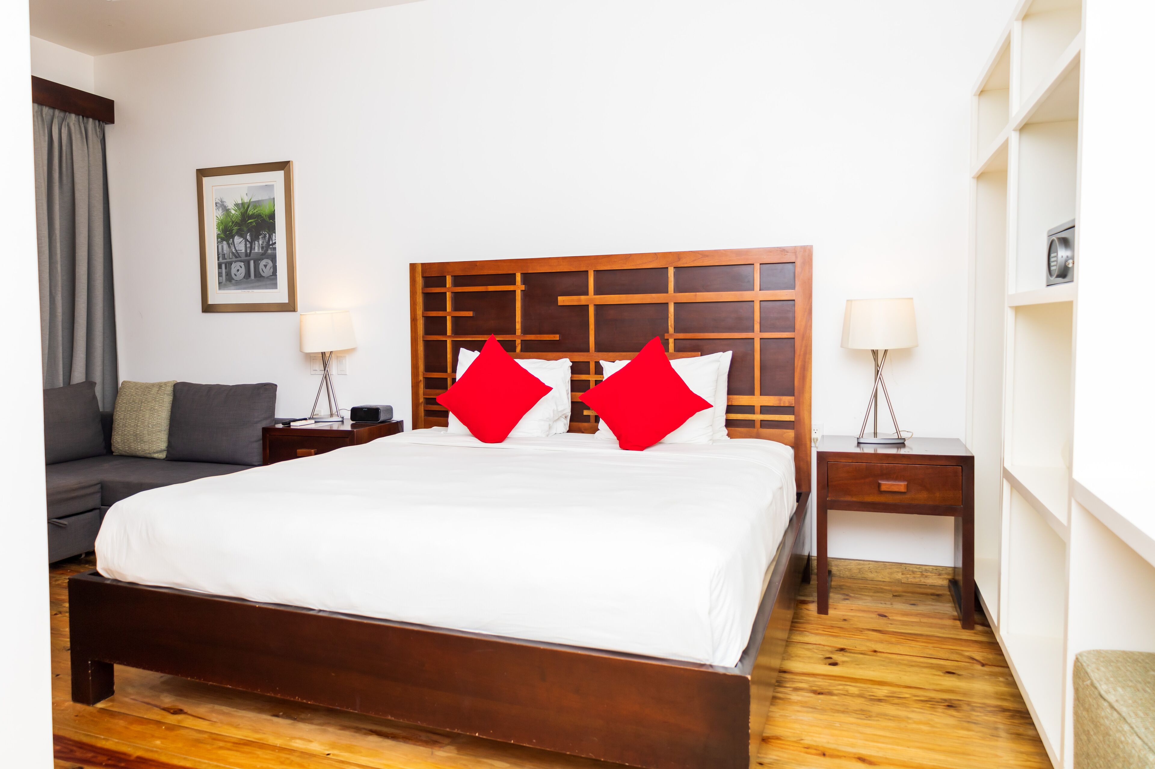 Una habitación de hotel con una cama grande, un cabecero de madera, una mesita de noche con una lámpara, un sofá y un cuadro enmarcado en la pared.