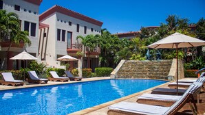 A swimming pool with lounge chairs and umbrellas, surrounded by a stone wall and lush greenery. - La Placita Inn (Roatan)