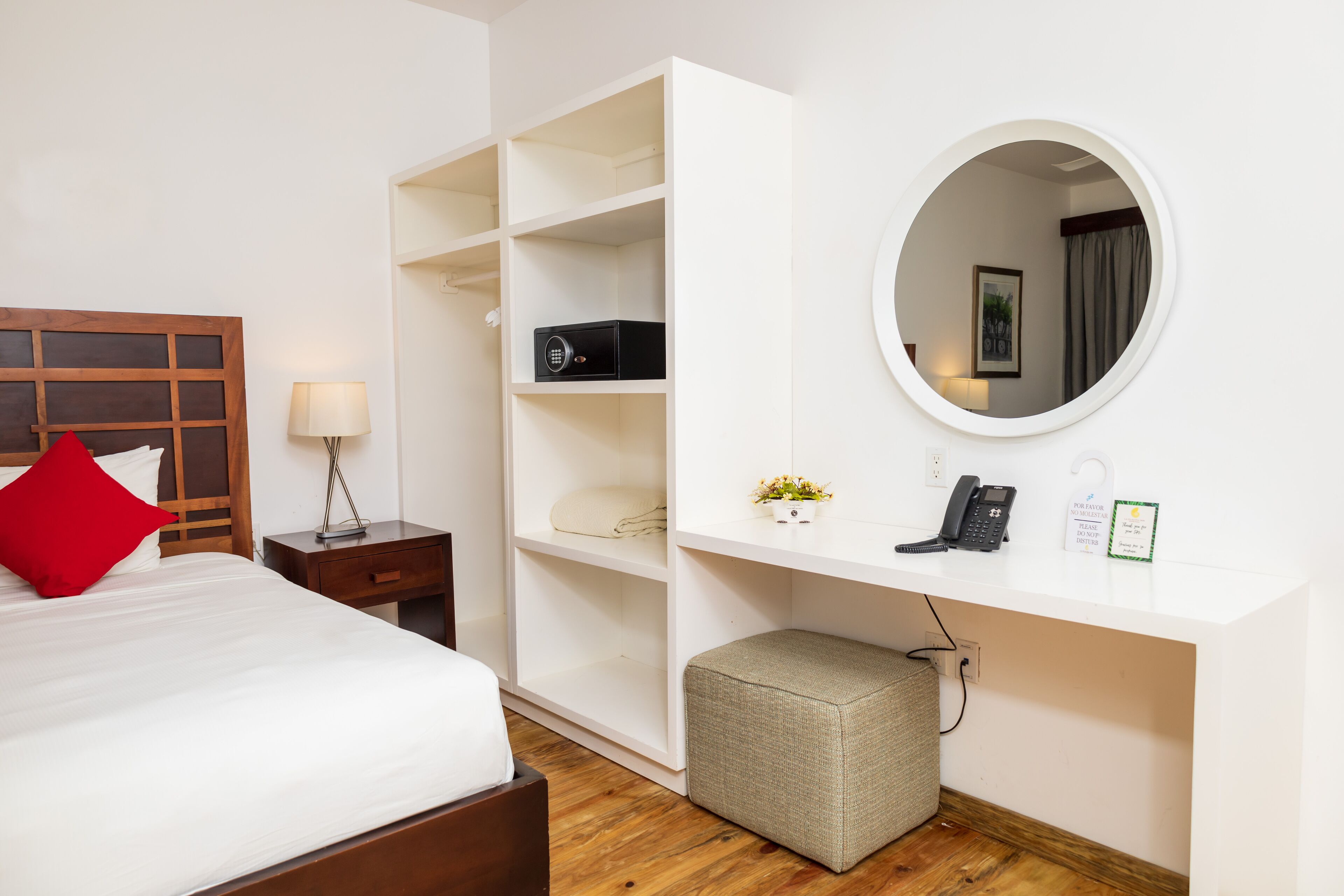 A hotel room with a bed, a nightstand, a desk with a mirror, a telephone, and a small plant.