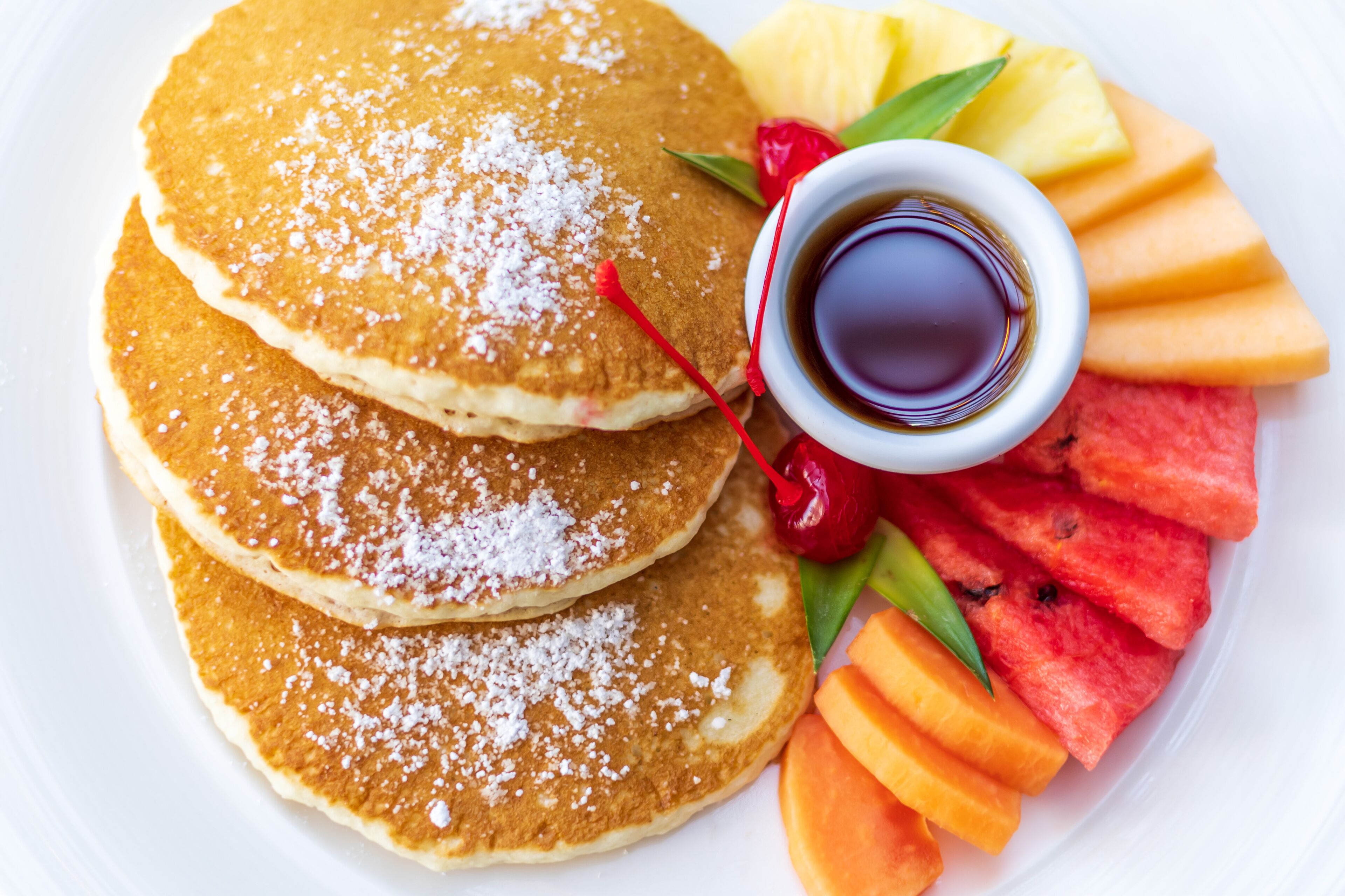 A plate of pancakes with syrup and fruit.