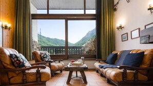 Una habitación con suelo de madera, dos sofás de cuero con cojines estampados, una mesa de centro de madera y un ventanal con vistas a la montaña.