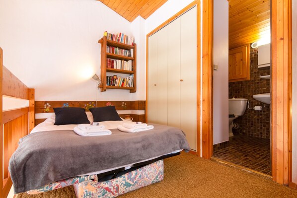 A bedroom with a bed, a bookshelf, a bathroom with a toilet and sink. - Les Soldanelles Cozy Alpine Apartment in Chamonix | Ski Access & Mountain Views, Le Tour (Argentière), France (Le Tour (Argentière))