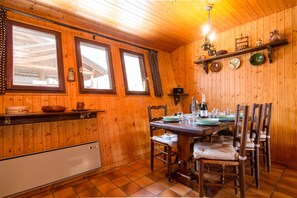 A wooden interior with a dining table set for four, chairs, a kitchen counter, and a shelf with dishes. - Les Soldanelles, Le Tour (Argentière), France (Le Tour (Argentière))