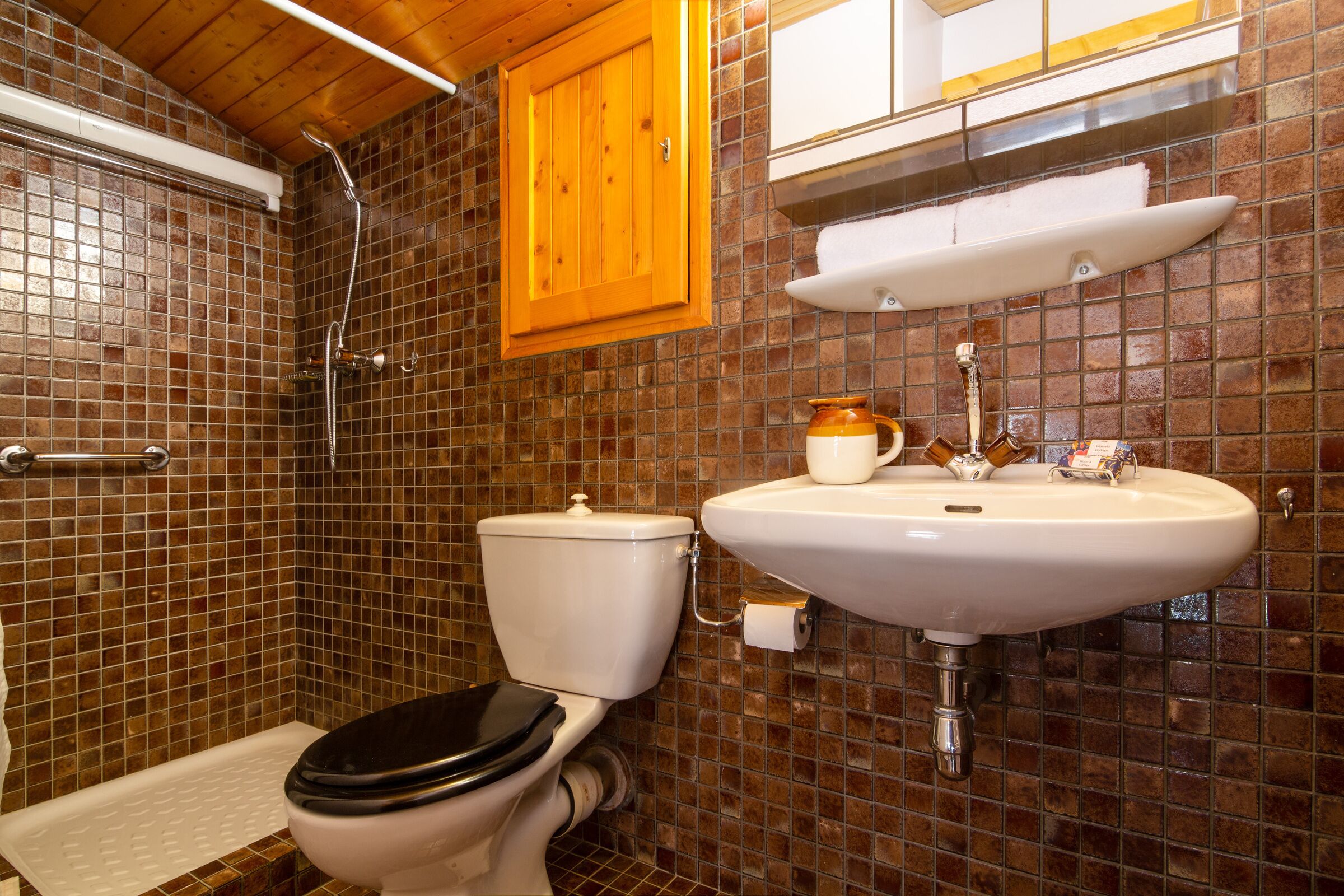 Een badkamer met een betegelde douche, toilet en wastafel met een beker en zeepdispenser.