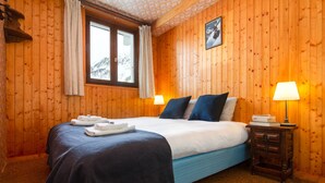 Una habitación con paneles de madera, una cama, dos lámparas de noche, un pequeño mesita de noche y una ventana con cortinas.