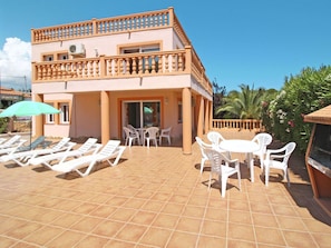 A two-story building with a balcony, outdoor seating area with chairs and tables, and a tiled patio.