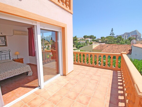A balcony with a view of a residential area, a bed with a floral bedspread, and a sliding glass door leading to an outdoor space.