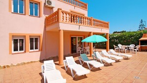 A two-story building with a balcony, outdoor seating area with white lounge chairs and a table, and a green umbrella. - Wonderful private villa for 11 people with private pool, A/C, WIFI, TV, terrace and pets allowed (Benissa)